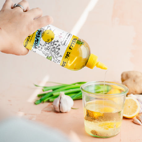 
                  
                    Hand squeezing Bella Del Sol Extra Virgin Olive Oil into a glass with lemon, garlic, and ginger – fresh salad dressing preparation scene
                  
                